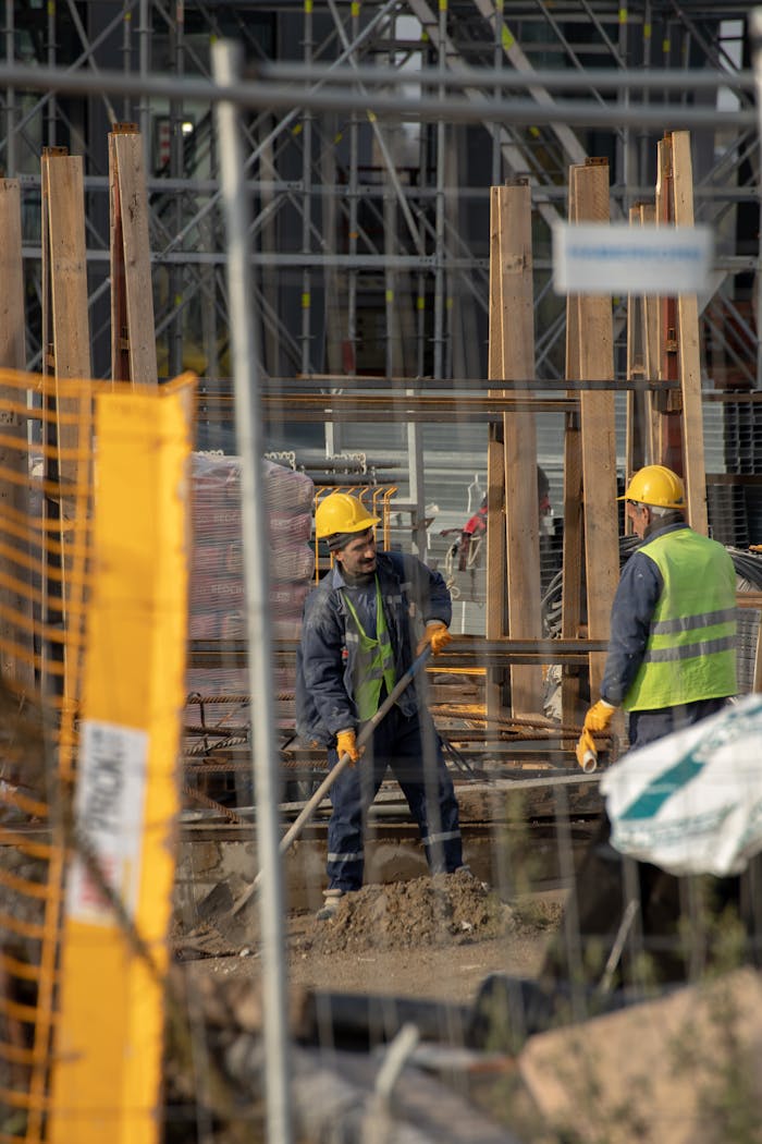 pexels photo 14367425 Construction workers in hard hats at an active building site with safety barriers.